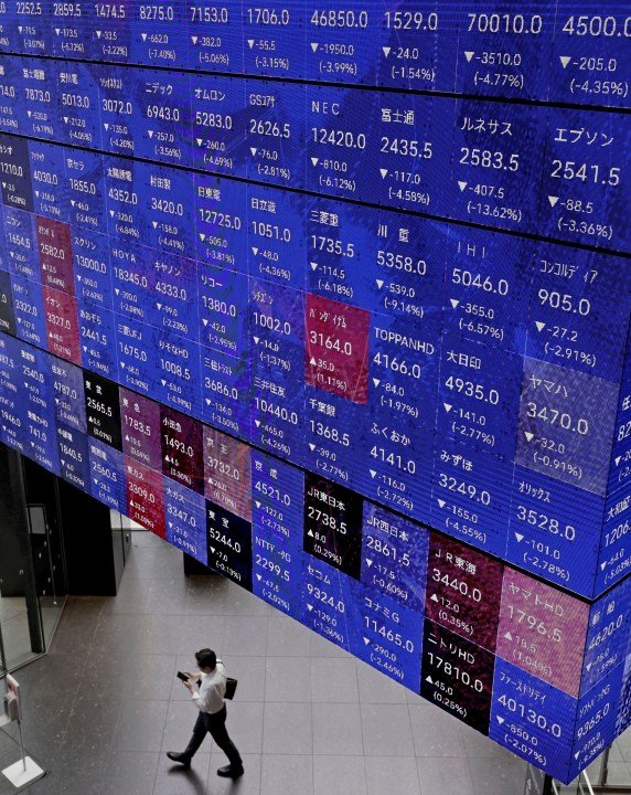 FILE - A person walks below an electronic stock board in Tokyo Thursday, July 25, 2024. Asian shares mostly declined in cautious trading Tuesday, July 30, ahead of central bank meetings around the world. (Kyodo News via AP, File)