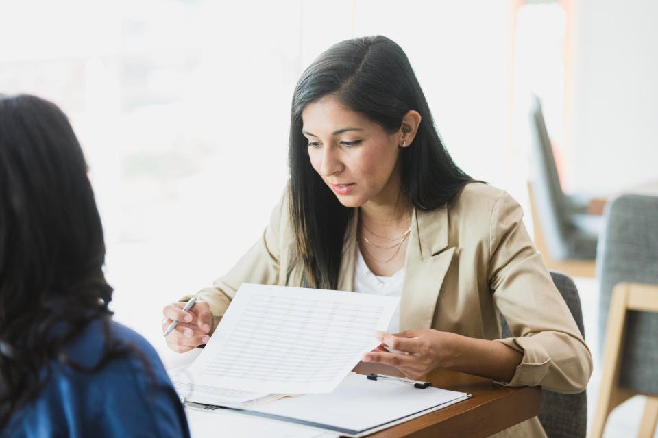 A mid adult businesswoman examines a spreadsheet during a meeting with a female colleague.